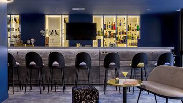 Una zona de bar con televisor de pantalla plana, varios taburetes, una mesa redonda con una copa de martini y un sofá.