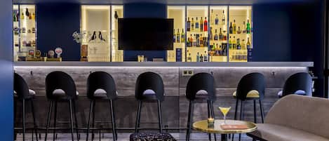 Uma área de bar com televisão de tela plana, vários bancos altos, uma mesa redonda com uma taça de martini e um sofá.