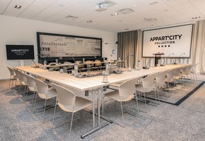 Una sala conferenze con un lungo tavolo, sedie, uno schermo per proiezioni e uno schermo per presentazioni.