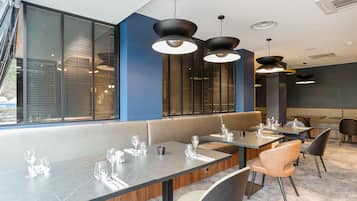 Een modern restaurant met een lange toonbank, meerdere tafels en een groot raam met zonwering.