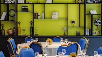 Un comedor con mesas dispuestas para el servicio, sillas con detalles dorados y estantes con diversos objetos decorativos.