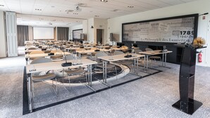 Un salón de conferencias con varias mesas y sillas, una pantalla grande y un proyector.