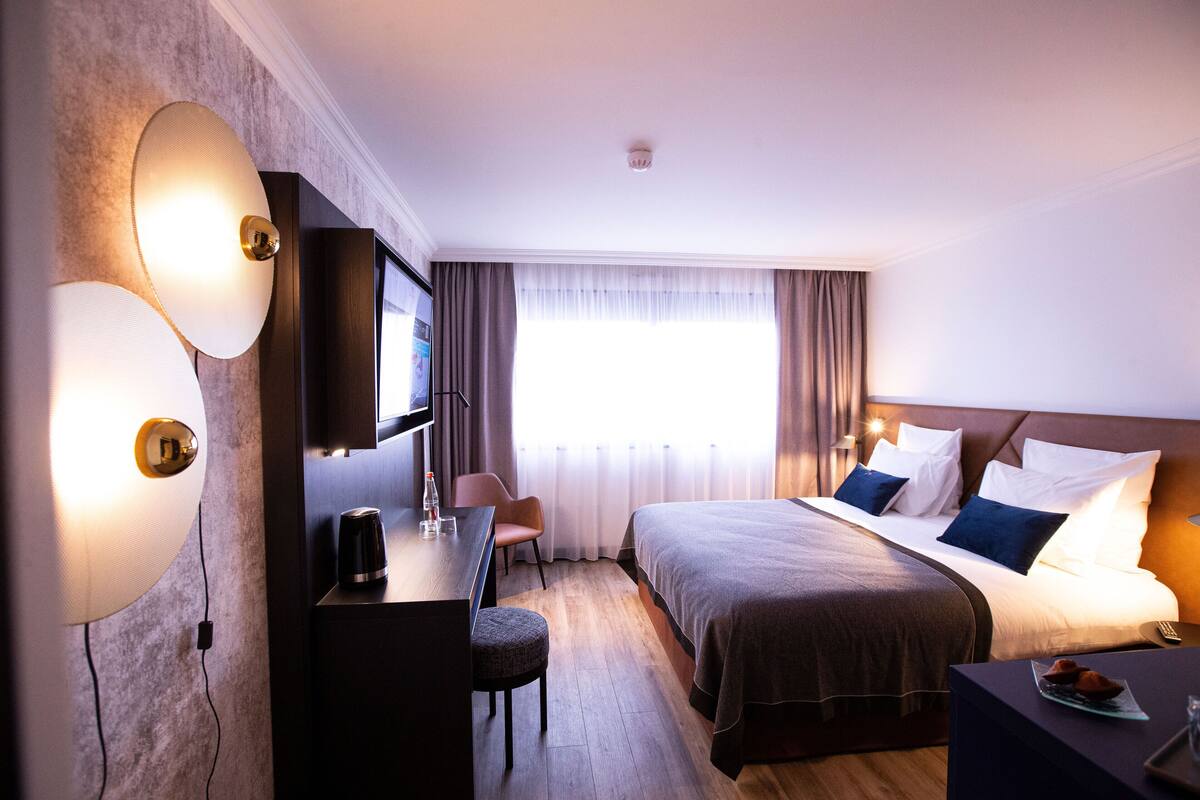 Une chambre d’hôtel avec un lit, un bureau, une chaise, une télévision et des rideaux.