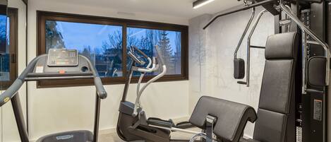 A gym with a treadmill, elliptical, and weight machine.