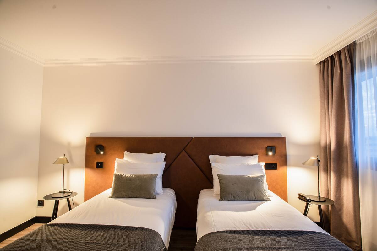 Une chambre d’hôtel avec deux lits, une tête de lit en bois, des lampes de chevet et une vue sur l’extérieur.