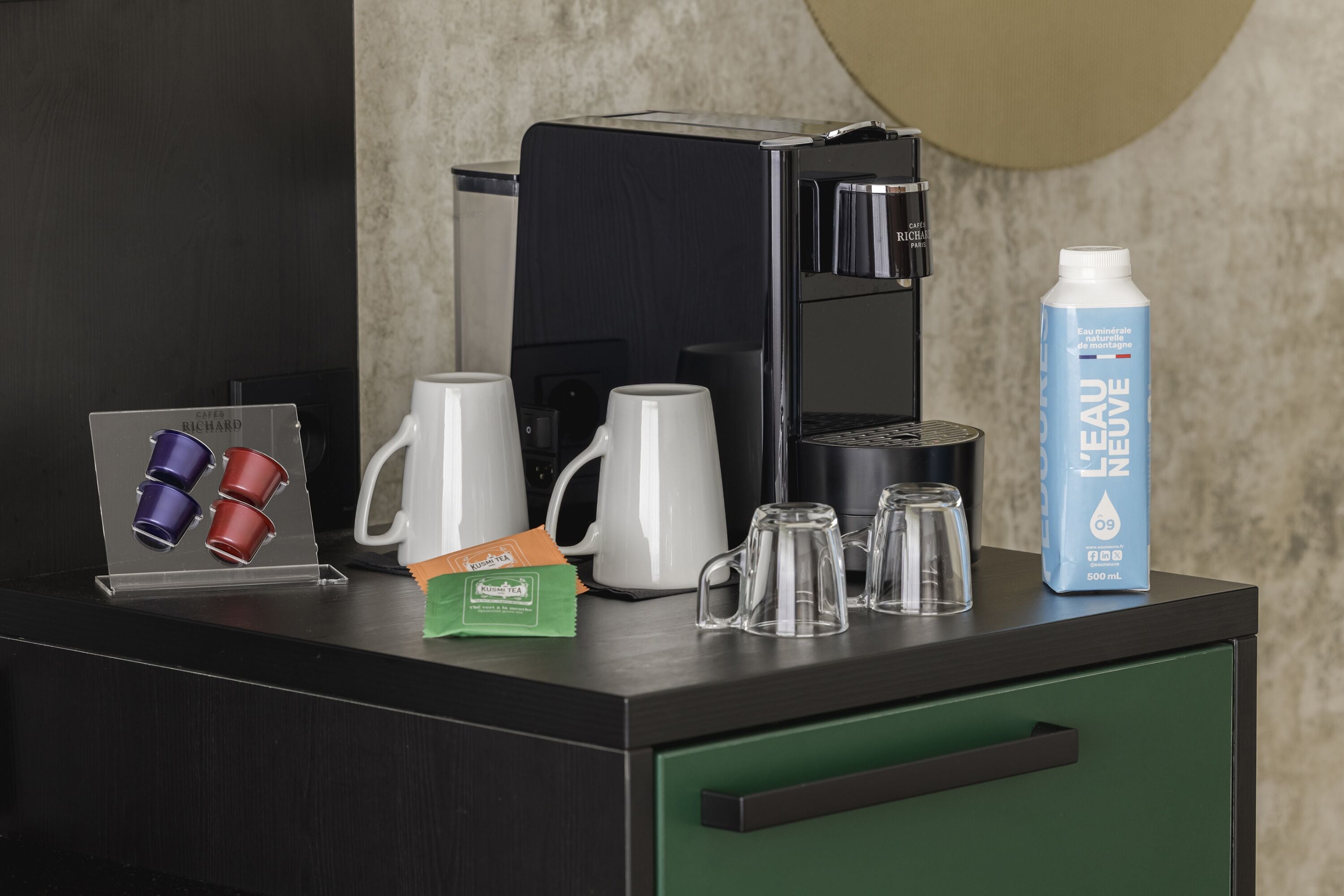 Eine Kaffeestation mit einer Kaffeemaschine, einer Wasserflasche und verschiedenen Tassen und Bechern.