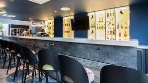 Una zona de bar con una barra larga, varios taburetes y una pantalla de televisión.