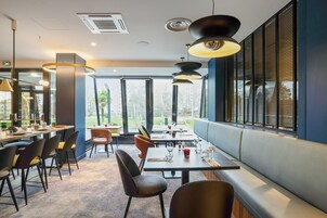 Un restaurante moderno con una barra alargada, varias mesas y una zona de estar con bancos.