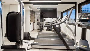 Un gimnasio con cintas de correr, bicicletas estáticas y una pantalla de televisión.