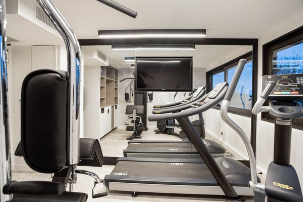 Una palestra con tapis roulant, cyclette e uno schermo televisivo.