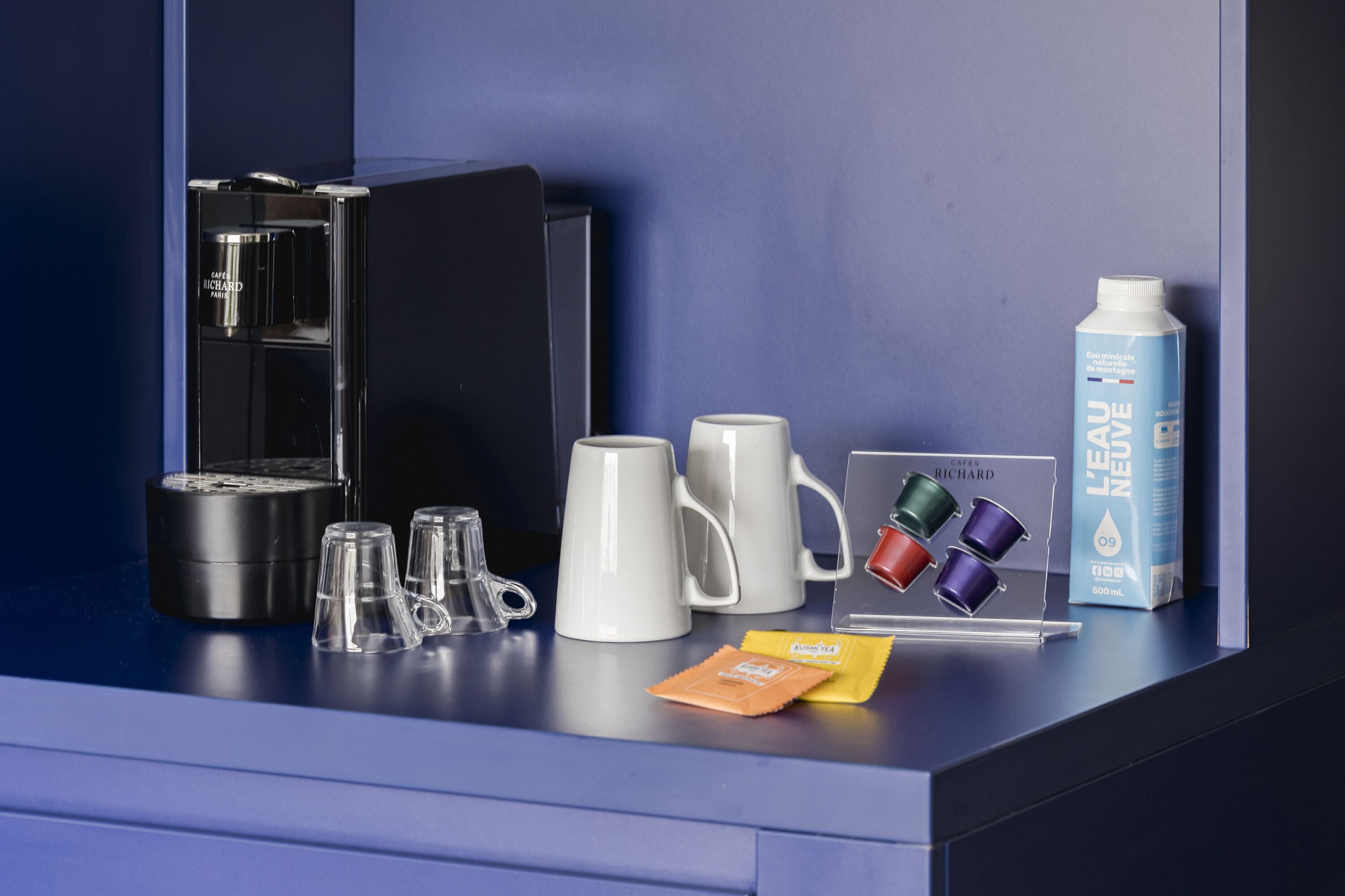 A coffee station with a coffee machine, mugs, and tea packets.