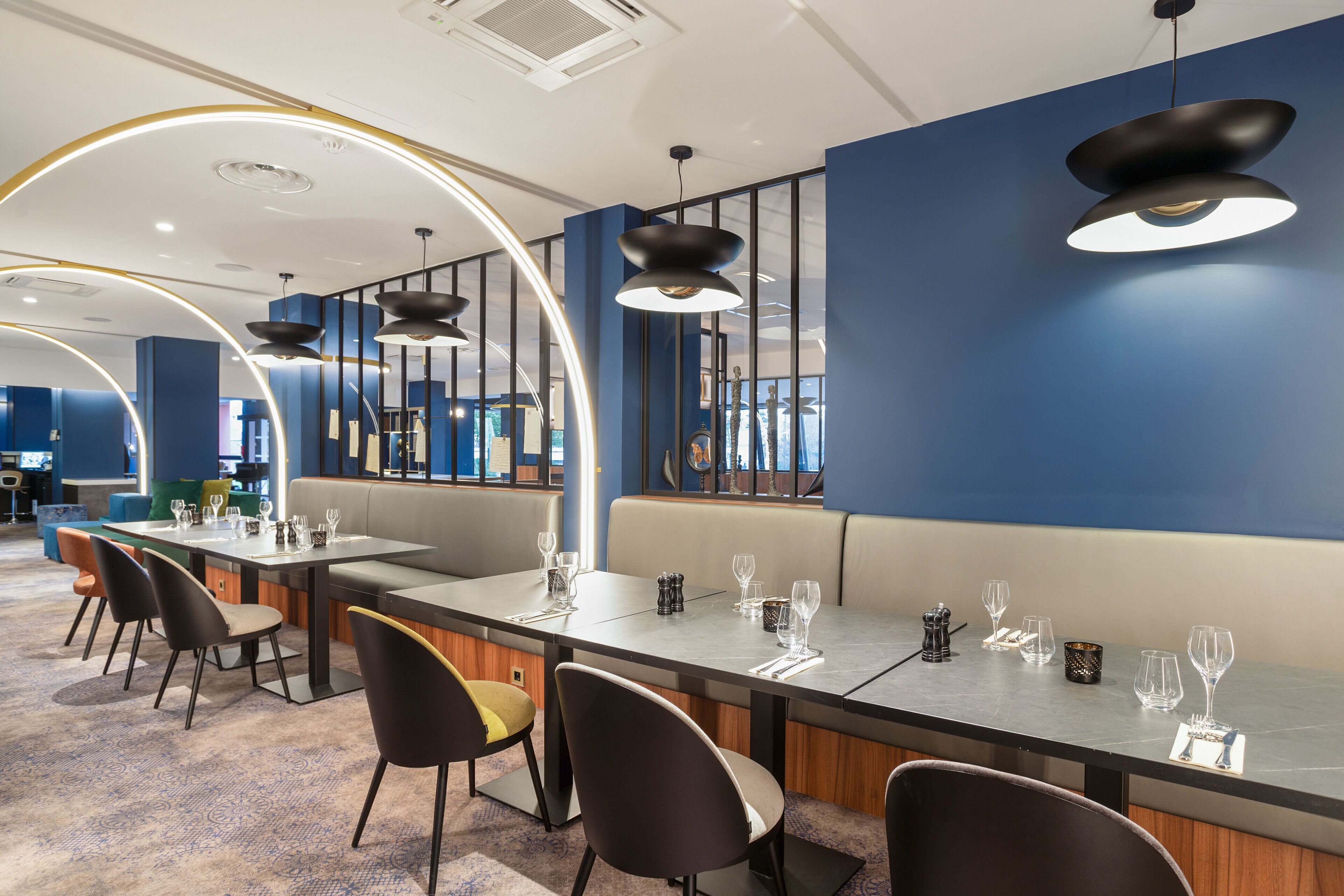 A modern restaurant with a long table set for dining, cushioned seating, and contemporary lighting fixtures.
