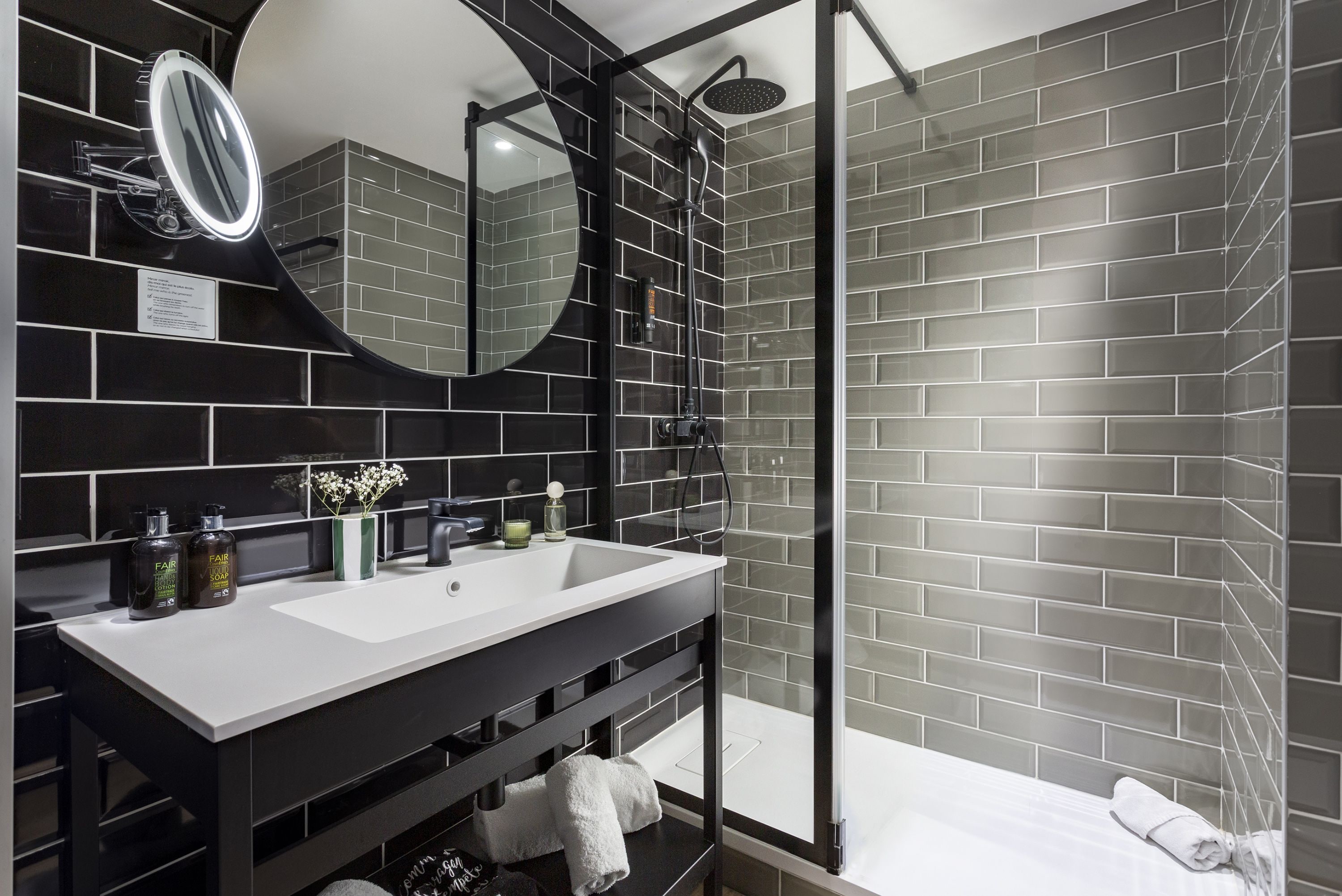 Un baño moderno con diseño de baldosas blanco y negro, un espejo grande, un lavabo y una zona de ducha.