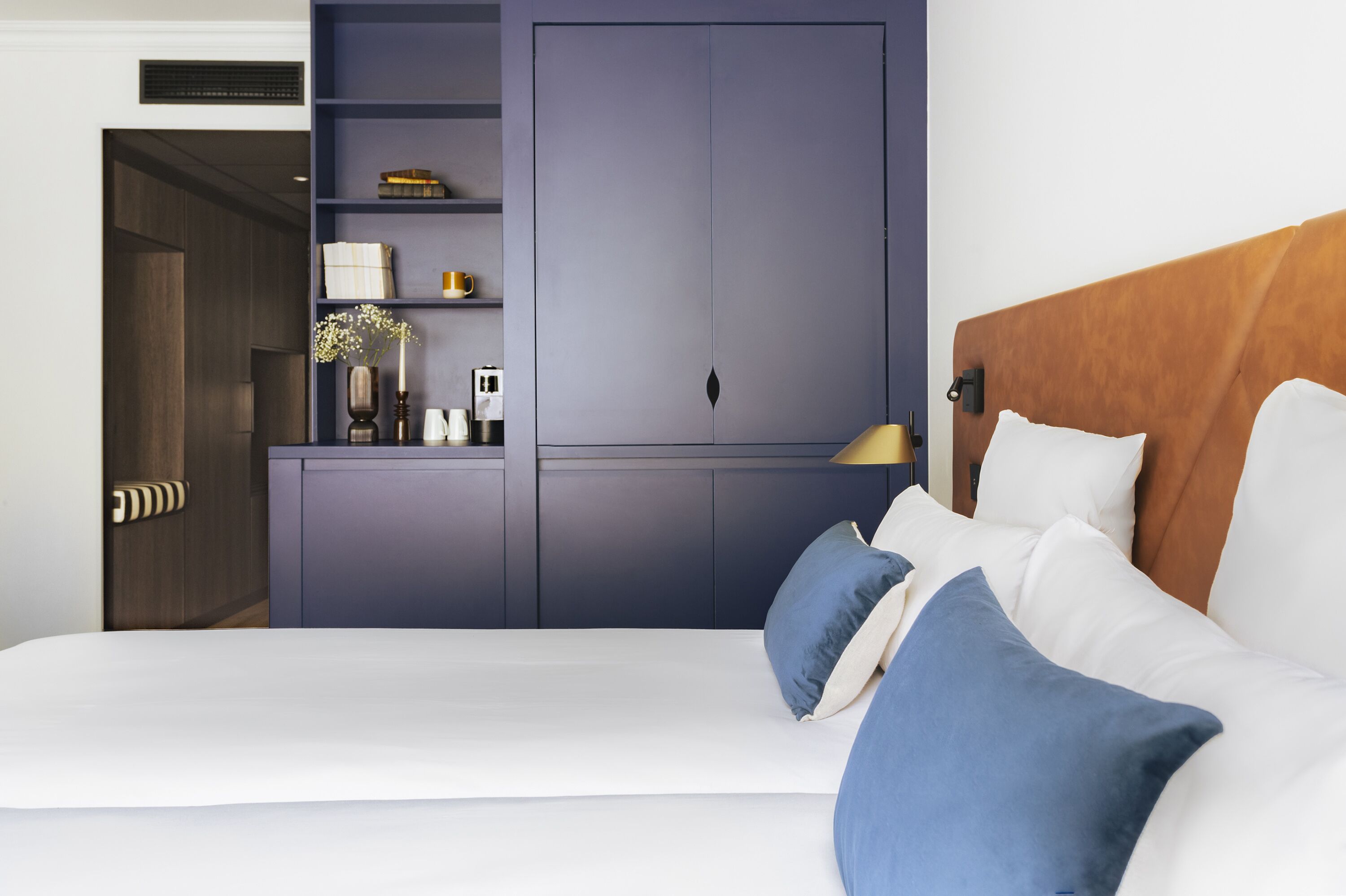 A hotel room with a bed, a wardrobe, and a bedside table with a lamp.