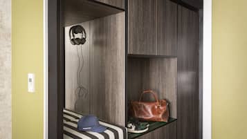 A room with a bed, a shelf with a handbag and shoes, and a wall-mounted thermostat.