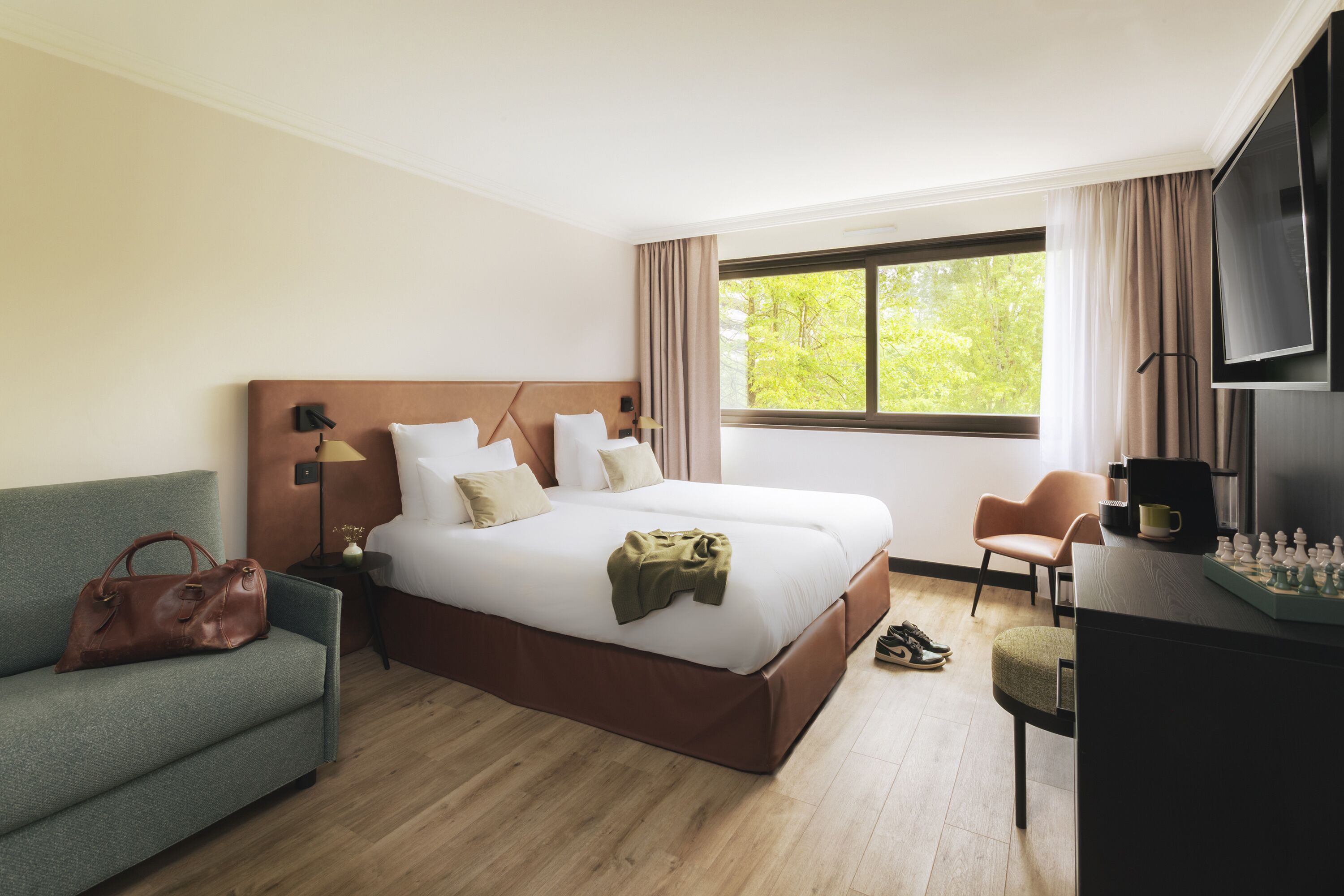 A hotel room with a bed, a sofa, a chair, a desk with a chessboard, and a TV.