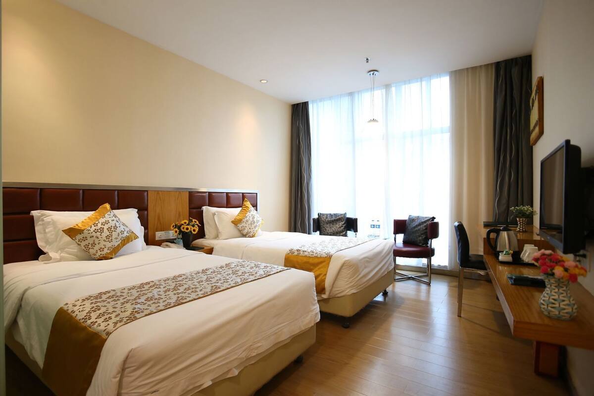 Une chambre d’hôtel avec deux lits, un bureau, une télévision et une grande fenêtre avec des rideaux.