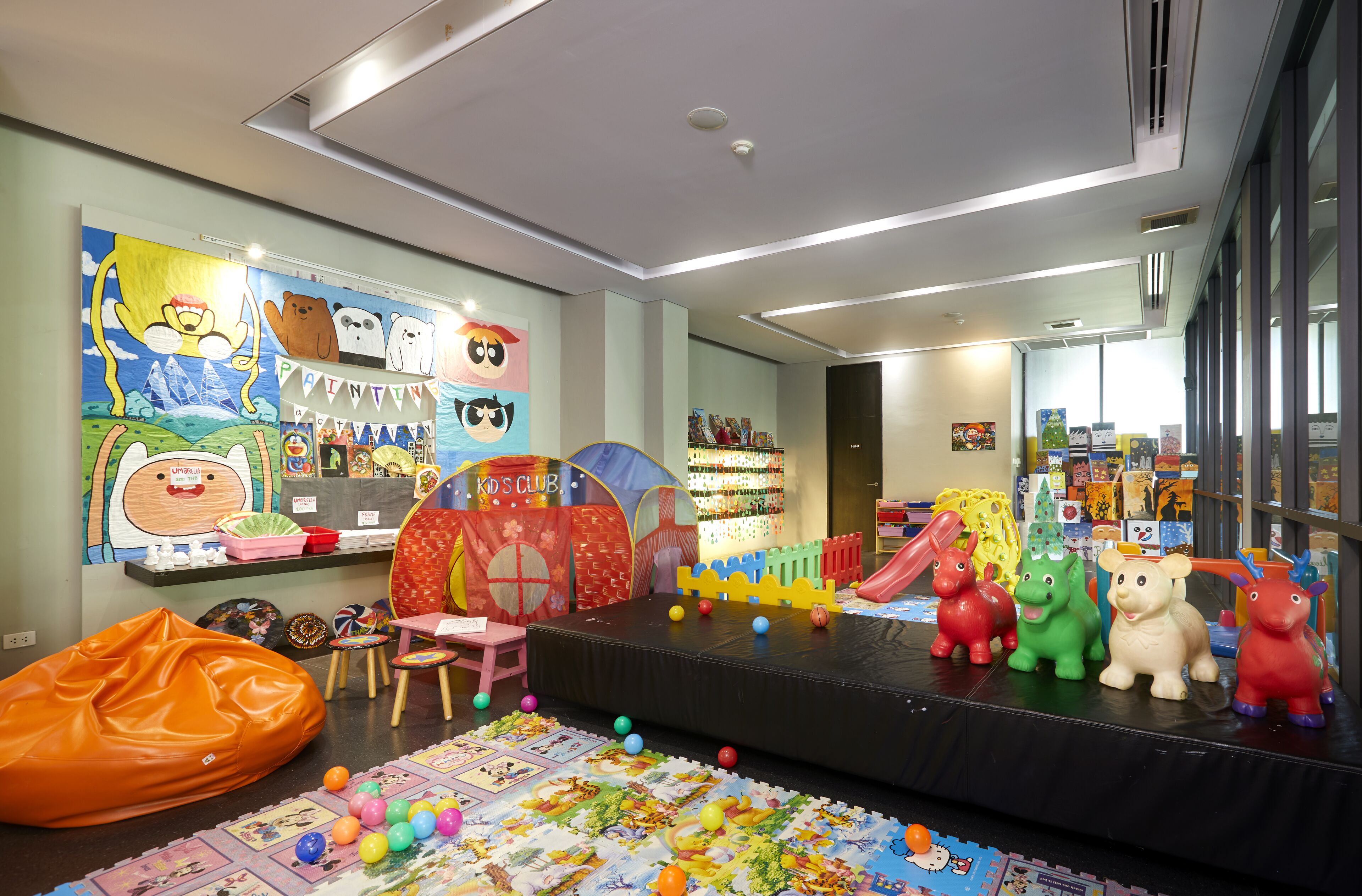 Un espace de jeux pour enfants comprenant une scène, des tapis de jeu colorés et divers jouets.