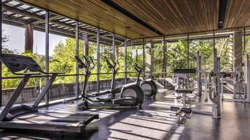A modern gym with cardio equipment, large windows, and a wooden ceiling.