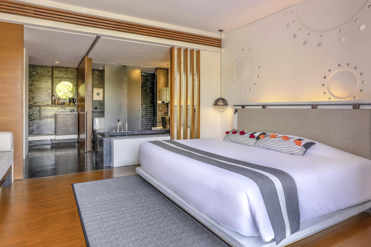 Ein modernes Hotelzimmer mit einem großen Bett, einer kleinen Küchenzeile und einem durch eine offene Tür einsehbarer Badezimmer.