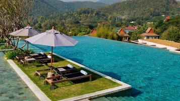 A swimming pool with lounge chairs and umbrellas, surrounded by a landscaped area and a view of hills.