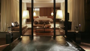 Habitación de hotel moderna con una cama grande, dos lámparas de noche, una mesita y vistas a través de un panel de vidrio.