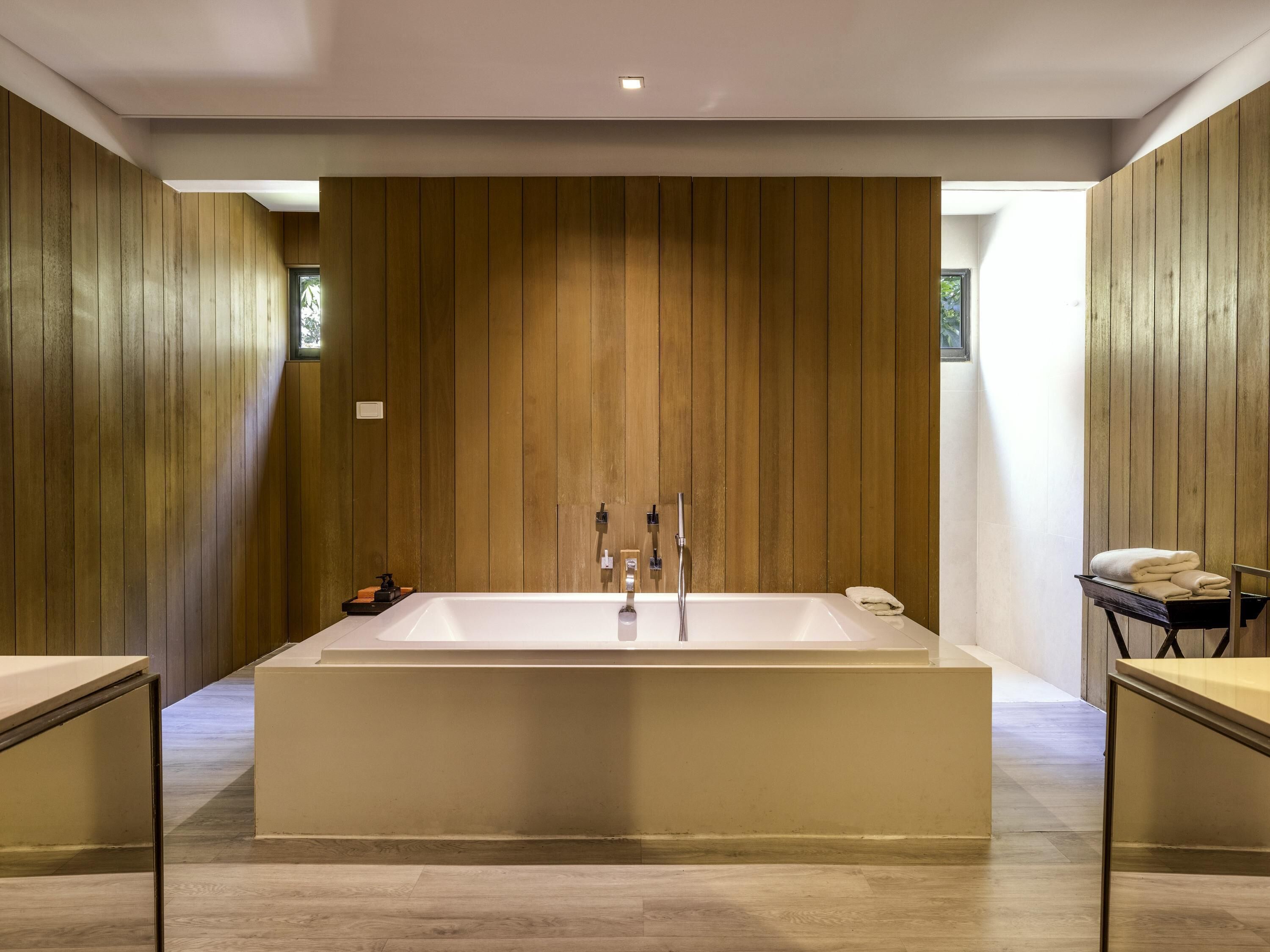 Ein modernes Badezimmer mit einer großen, freistehenden Badewanne, Holzpaneele an den Wänden und einem kleinen Tisch mit Handtüchern.