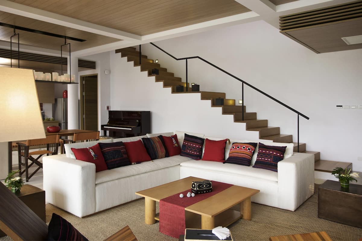 Ein modernes Wohnzimmer mit einem weißen Sofa, einem Holztisch, einem Klavier und einer Treppe.