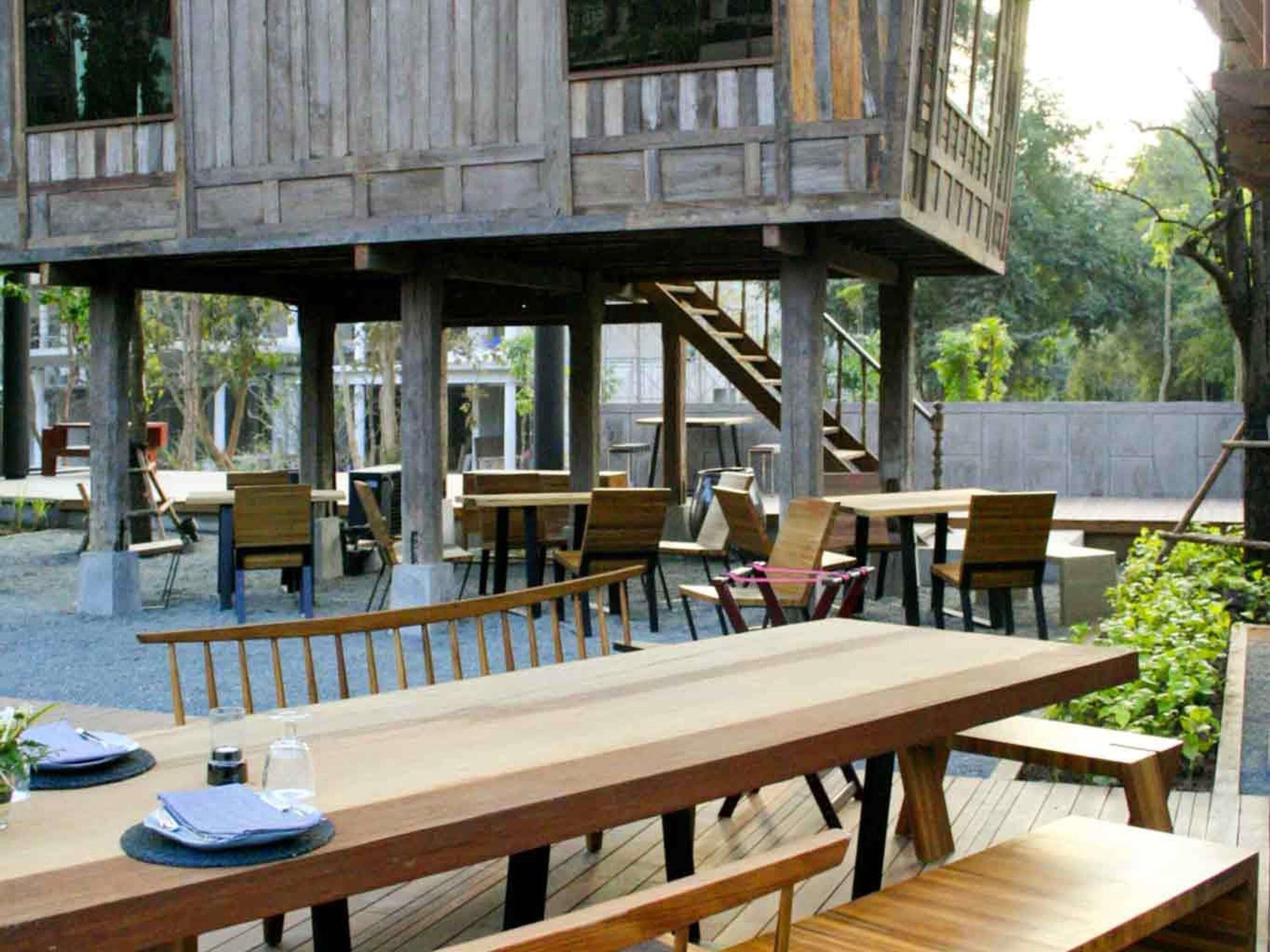 A wooden deck with tables and chairs, a staircase, and a view of trees.