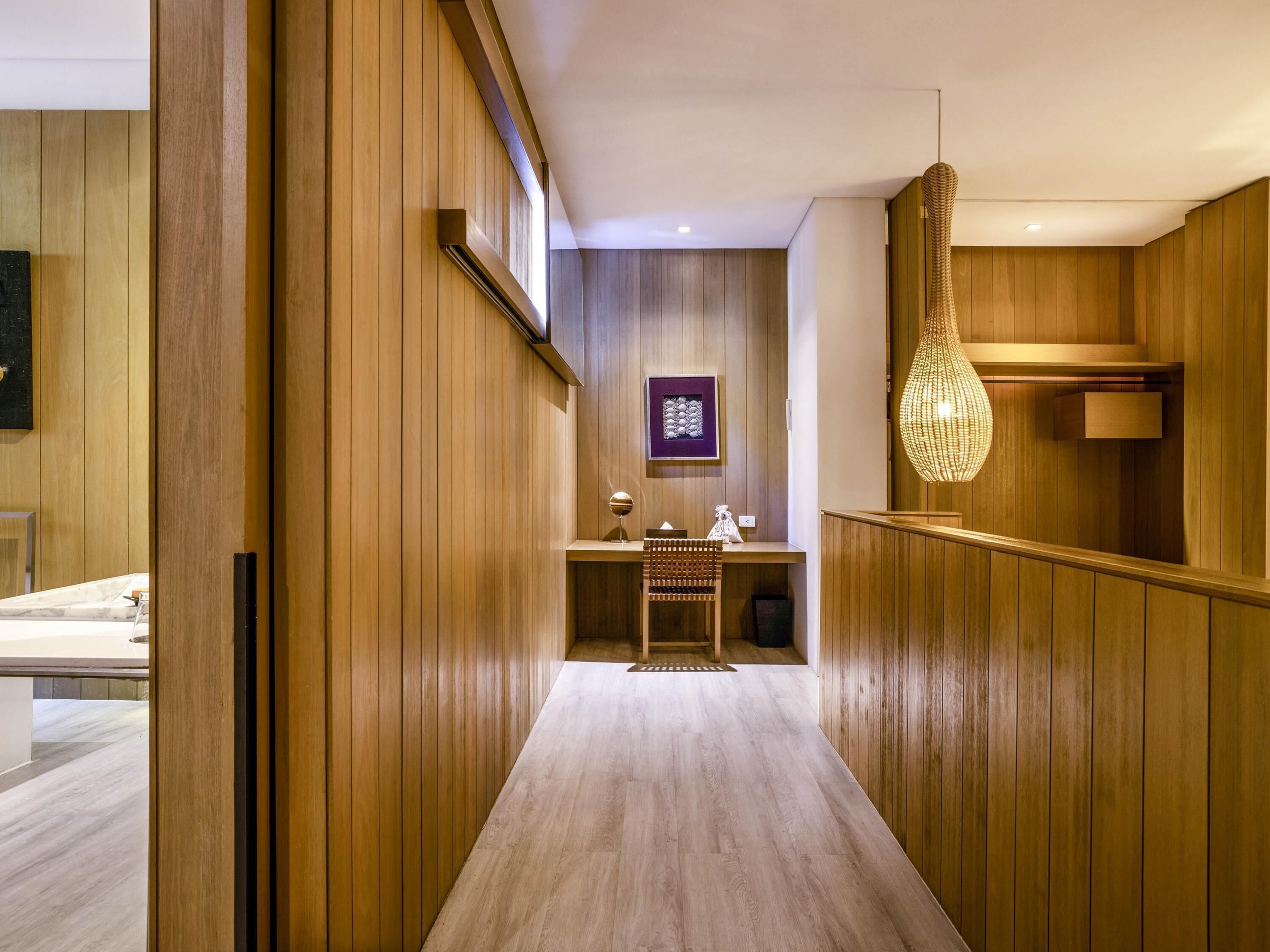A hallway with wooden paneling, a desk with a chair, a hanging light fixture, and a framed picture on the wall.