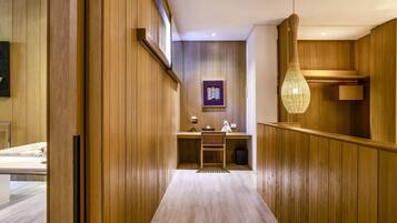 A hallway with wooden paneling, a desk with a chair, a hanging light fixture, and a framed picture on the wall.