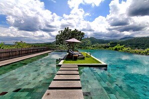 Una piscina cristalina con un deck de madera que conduce a una zona verde con un banco y una sombrilla.