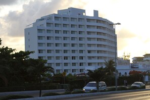 A multi-story hotel with a curved facade, a pedestrian crossing sign, and a street with parked cars and palm trees. - Calypso Hotel Cancun (Cancun)