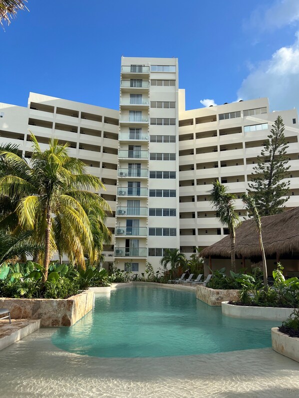 A modern hotel with a large pool, surrounded by palm trees and a thatched-roof structure. - Calypso Hotel Cancun (Cancun)