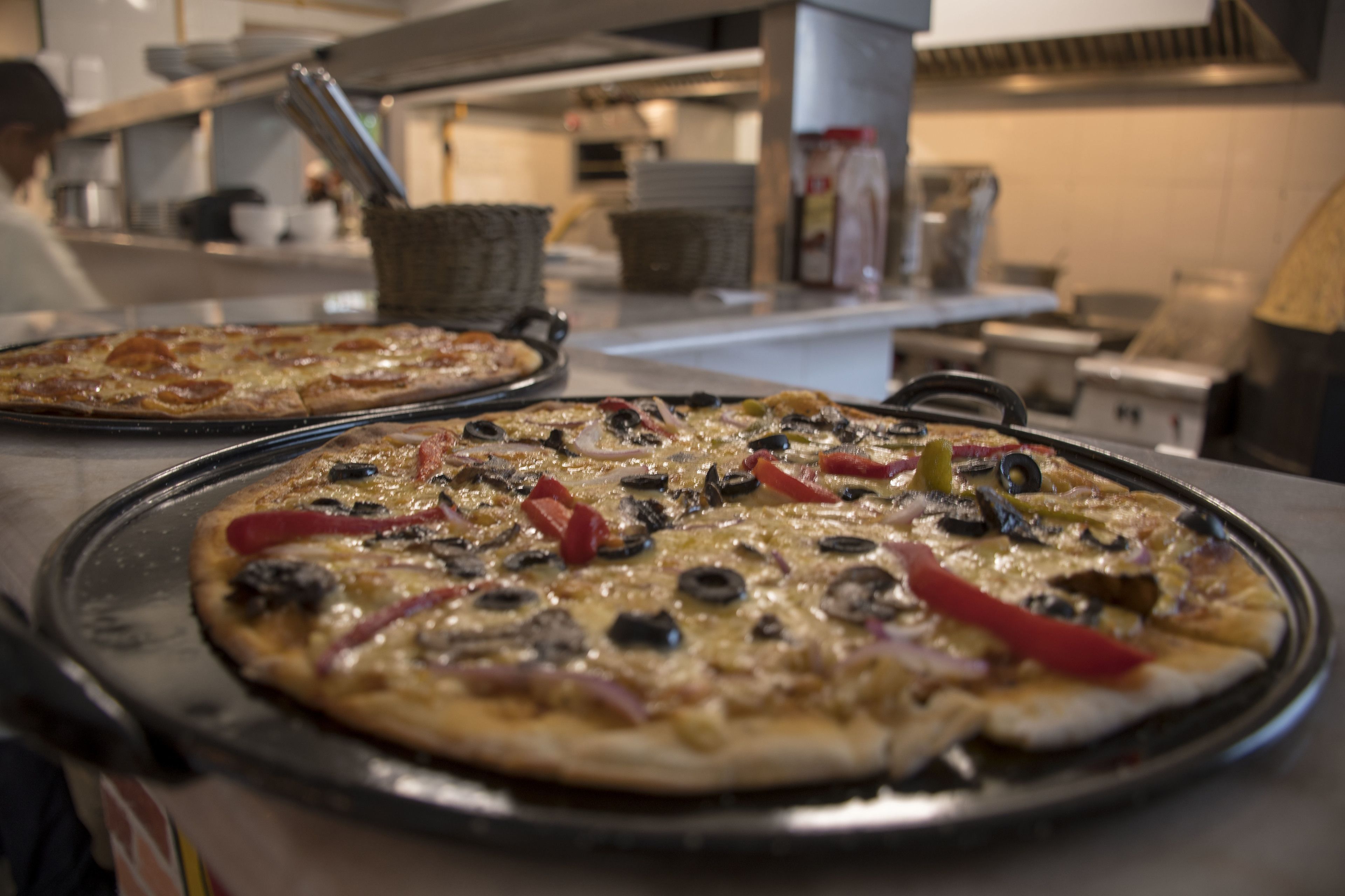Zwei Pizzen auf Metalltabletts in einer Küche.