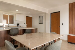 Una cocina moderna con una isla central, un comedor con una mesa grande y sillas, y armarios de madera.