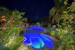 A swimming pool with blue lighting, surrounded by lush greenery and palm trees. - Calypso Hotel Cancun (Cancun)