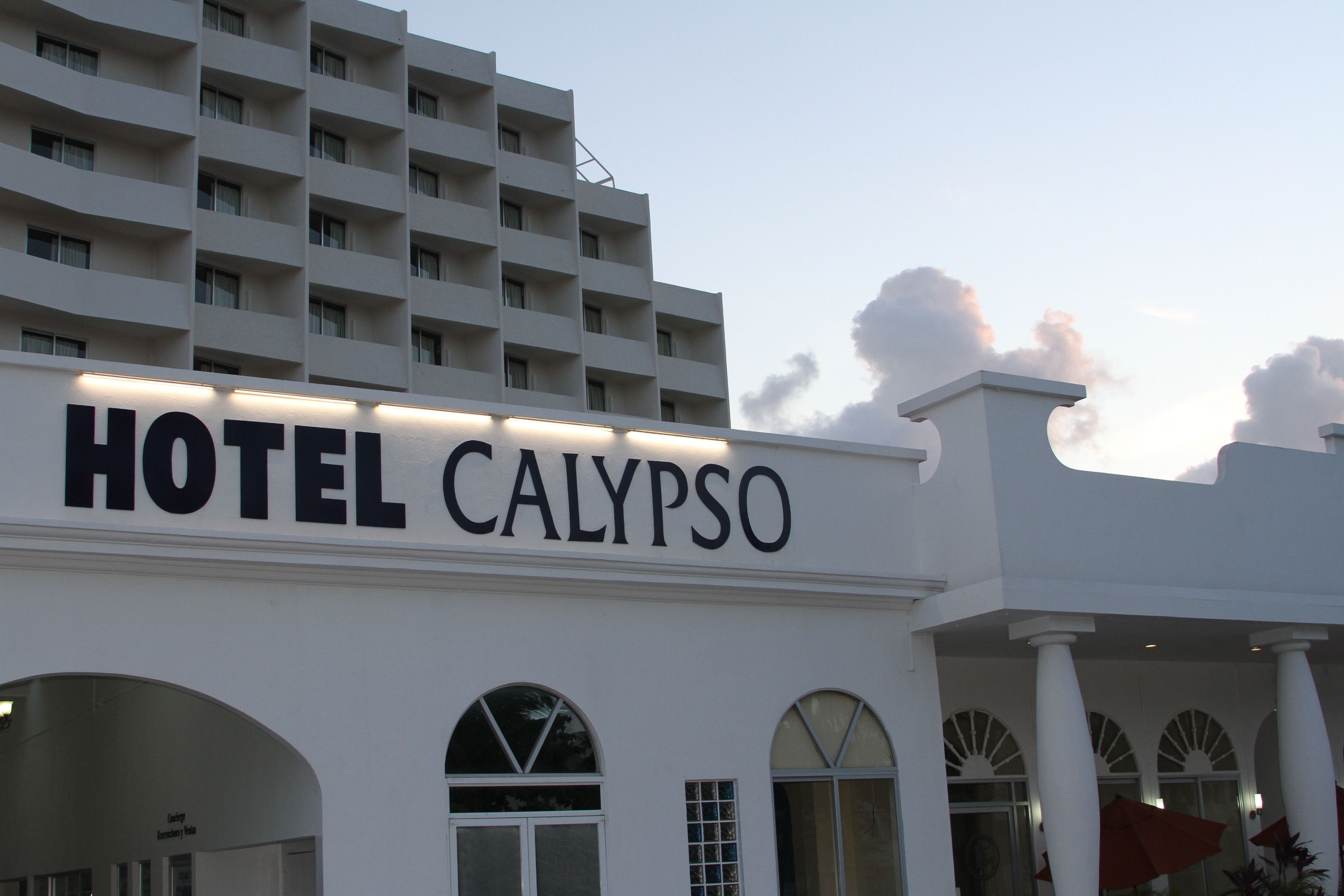 Un hotel llamado "HOTEL CALYPSO" con una fachada moderna, grandes ventanales y una entrada destacada.