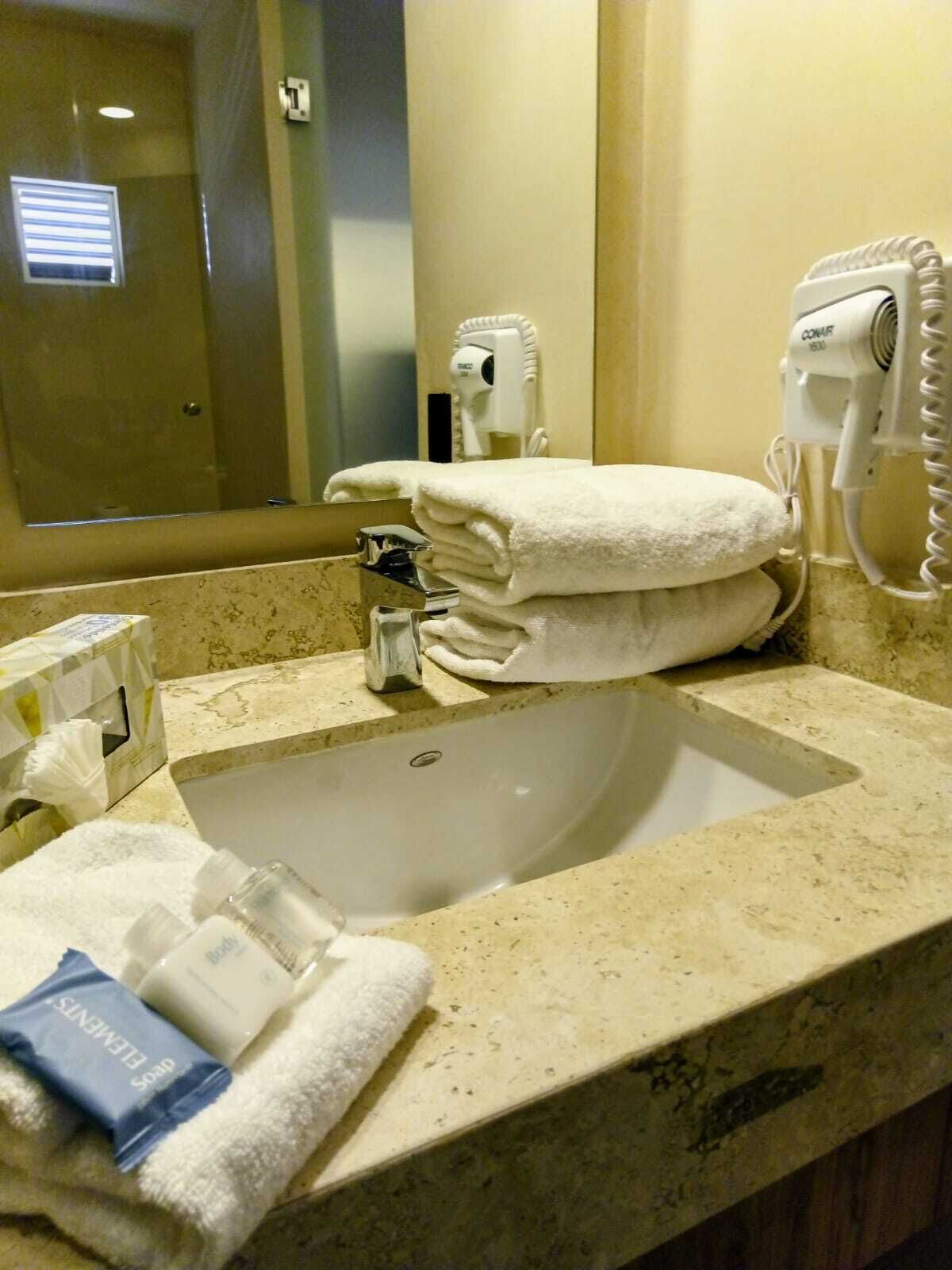 A hotel bathroom with a sink, towel dispenser, and hand dryer.