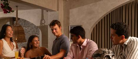 A group of people dining at a restaurant with a rustic interior, including stone walls and a hanging light fixture.