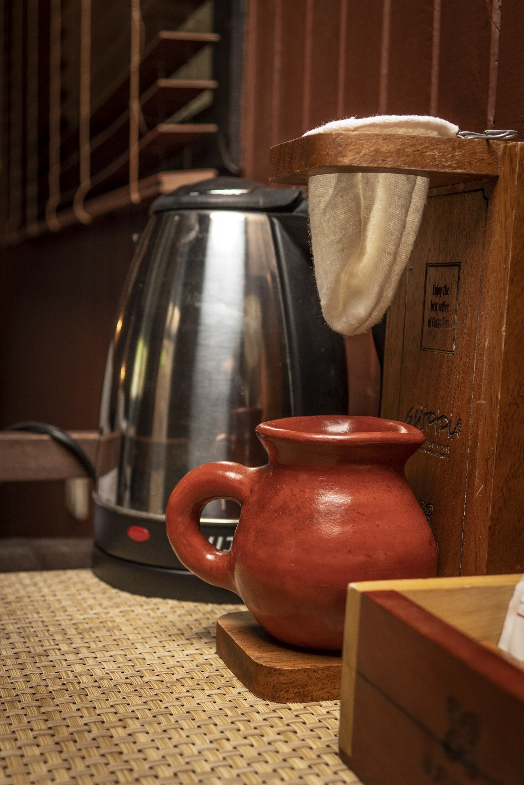 A kitchen area with a coffee maker, a red ceramic jug, and a woven mat on the floor.