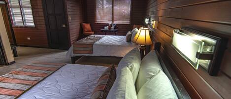 A room with two beds, a small table with a lamp, and a window with blinds.