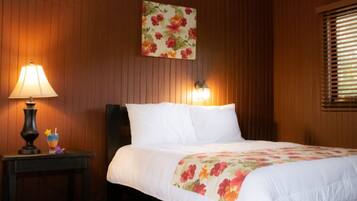 A hotel room with a bed, a nightstand, a lamp, a wall-mounted light, and a window with blinds.