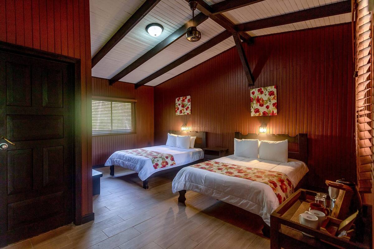 Une chambre avec deux lits, un plancher en bois, une porte en bois et un ventilateur de plafond.
