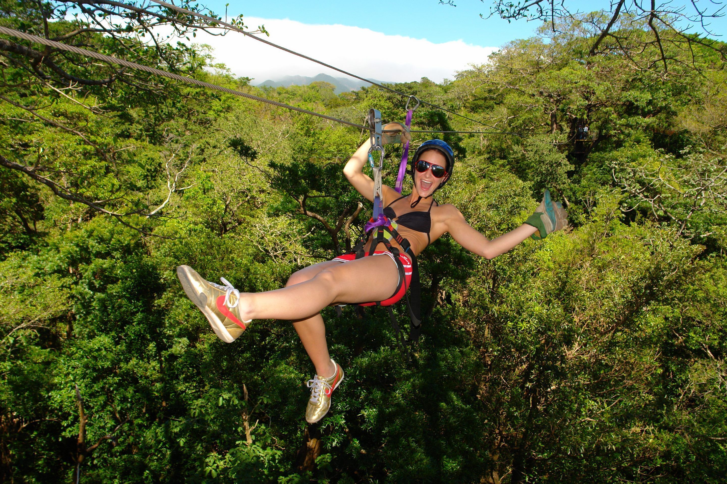 A person zip-lining through a forested area with dense greenery and trees.