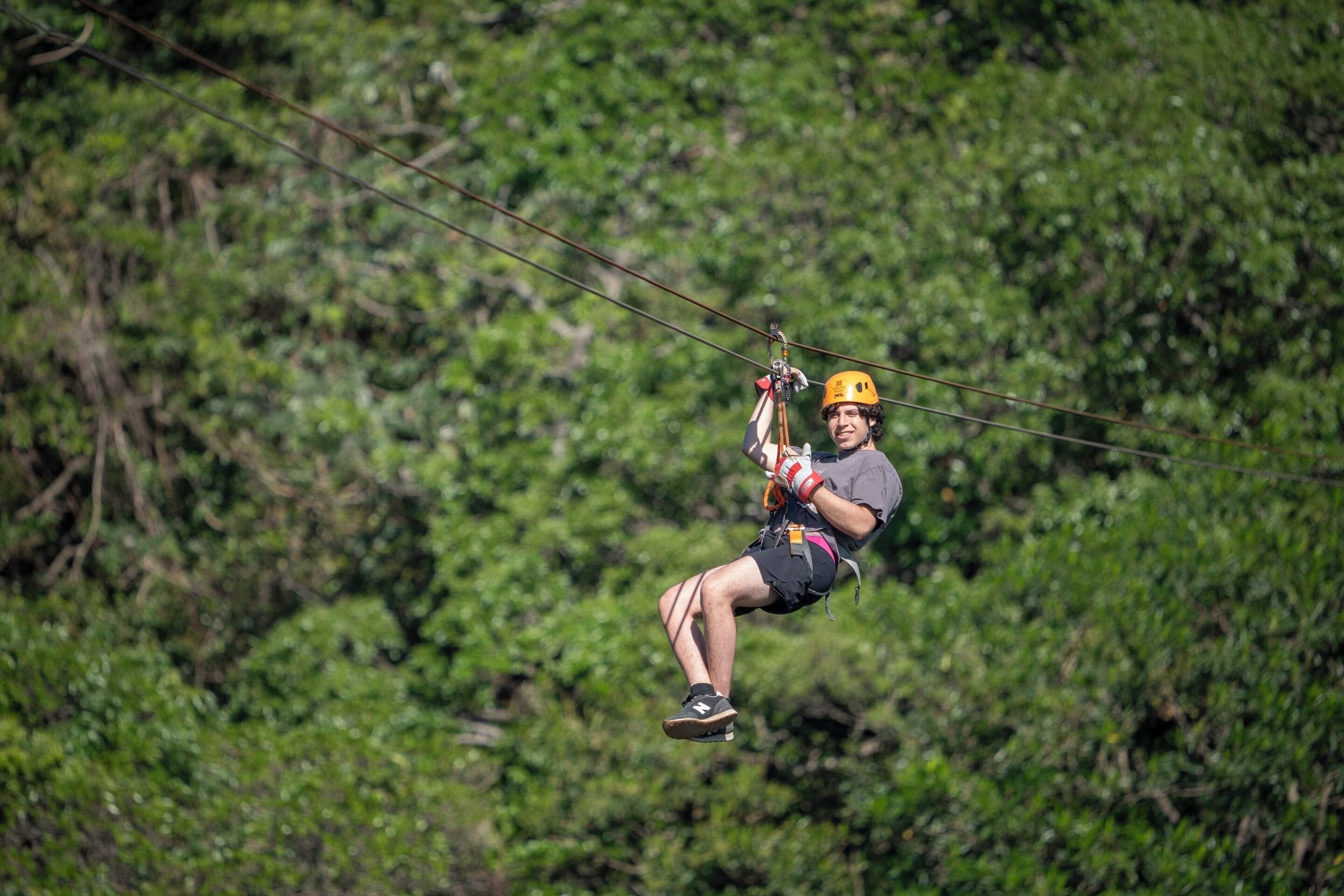 Una persona haciendo tirolesa, con casco y arnés, sobre un fondo natural de bosque verde.