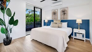 A bedroom with a bed, bedside tables, a ceiling fan, and a view of greenery through a sliding door. - Elysium Apartments (Palm Cove)