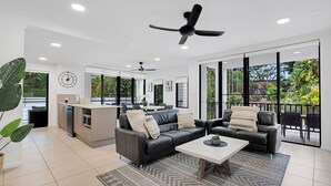 A spacious living area with a modern kitchen, large windows, and a ceiling fan. - Elysium Apartments (Palm Cove)