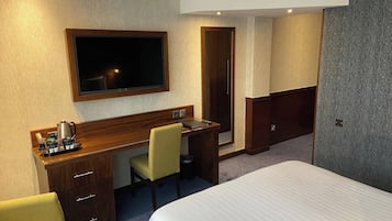 A hotel room with a bed, a desk with a chair, a television, and a minibar.