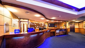 Un'area reception di un hotel con una scrivania a reception curva, una sezione 'Purses Desk', un cartello 'Conferge' e un deposito bagagli.